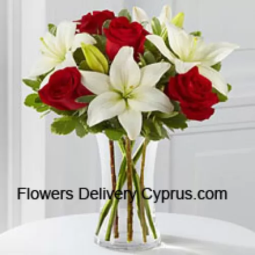 Roses rouges et lys blancs avec quelques remplissages saisonniers dans un vase en verre